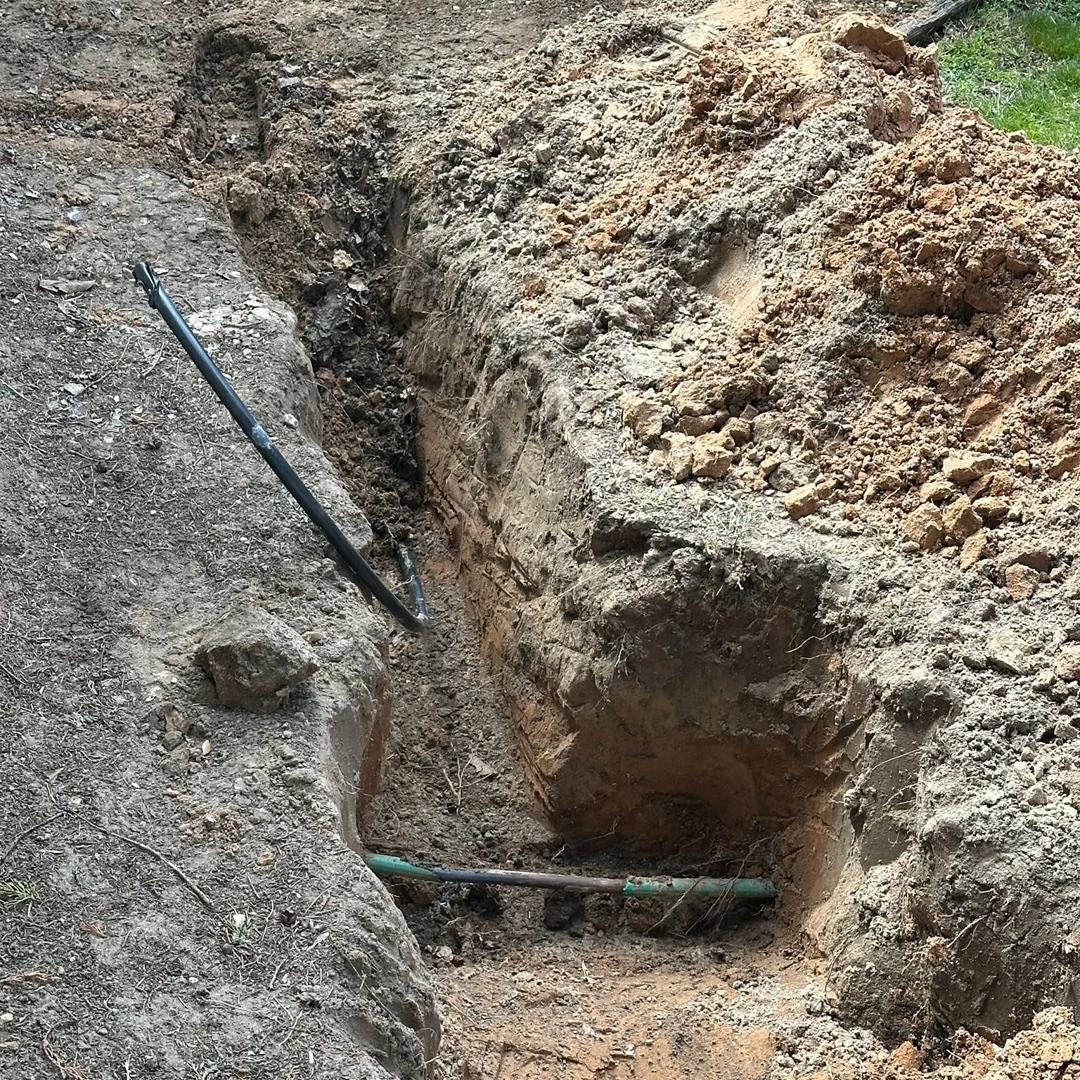 Close view of the open trench with new poly pipe laid alongside the old line