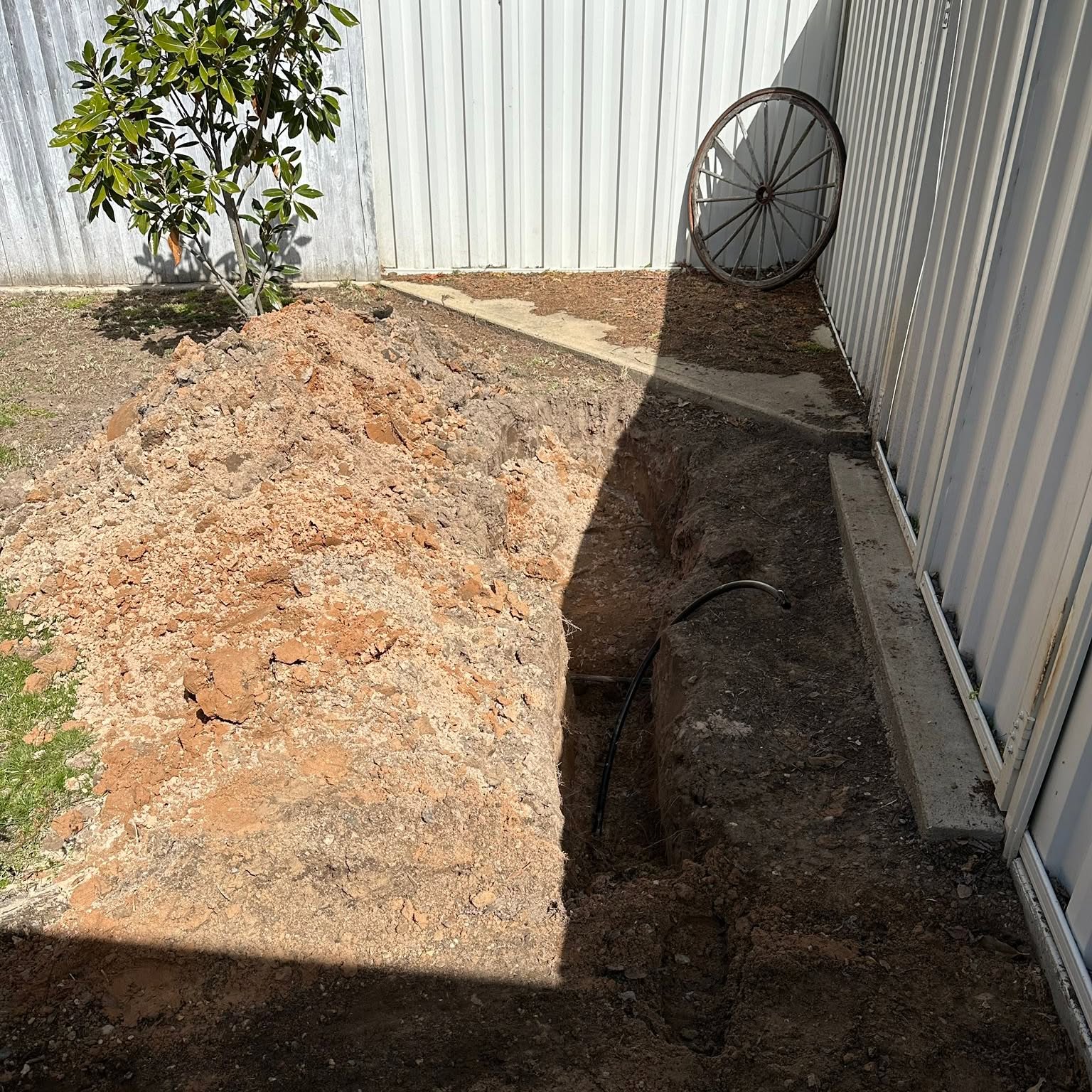 Trench alongside a shed wall with the new pipe run in place